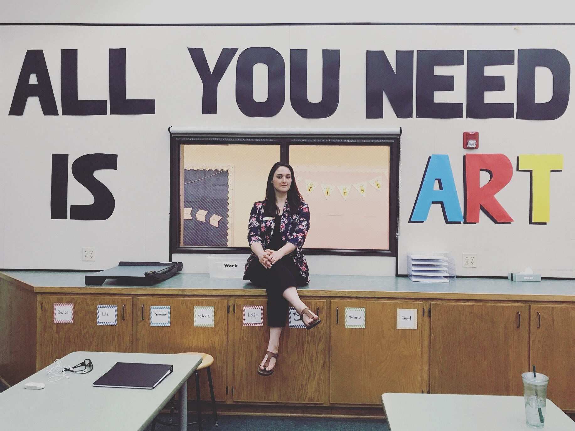 photograph of Julie sitting down in front of words that read 'all you need is art'.