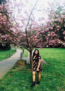 photograph of Jomilyn smiling in a black dress, standing in front of a flowering tree