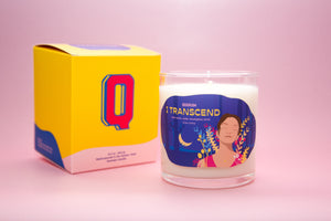 Photograph of the I Transcend affirmation candle. Photo is on a pink background and the candle is next to a bright yellow product box.