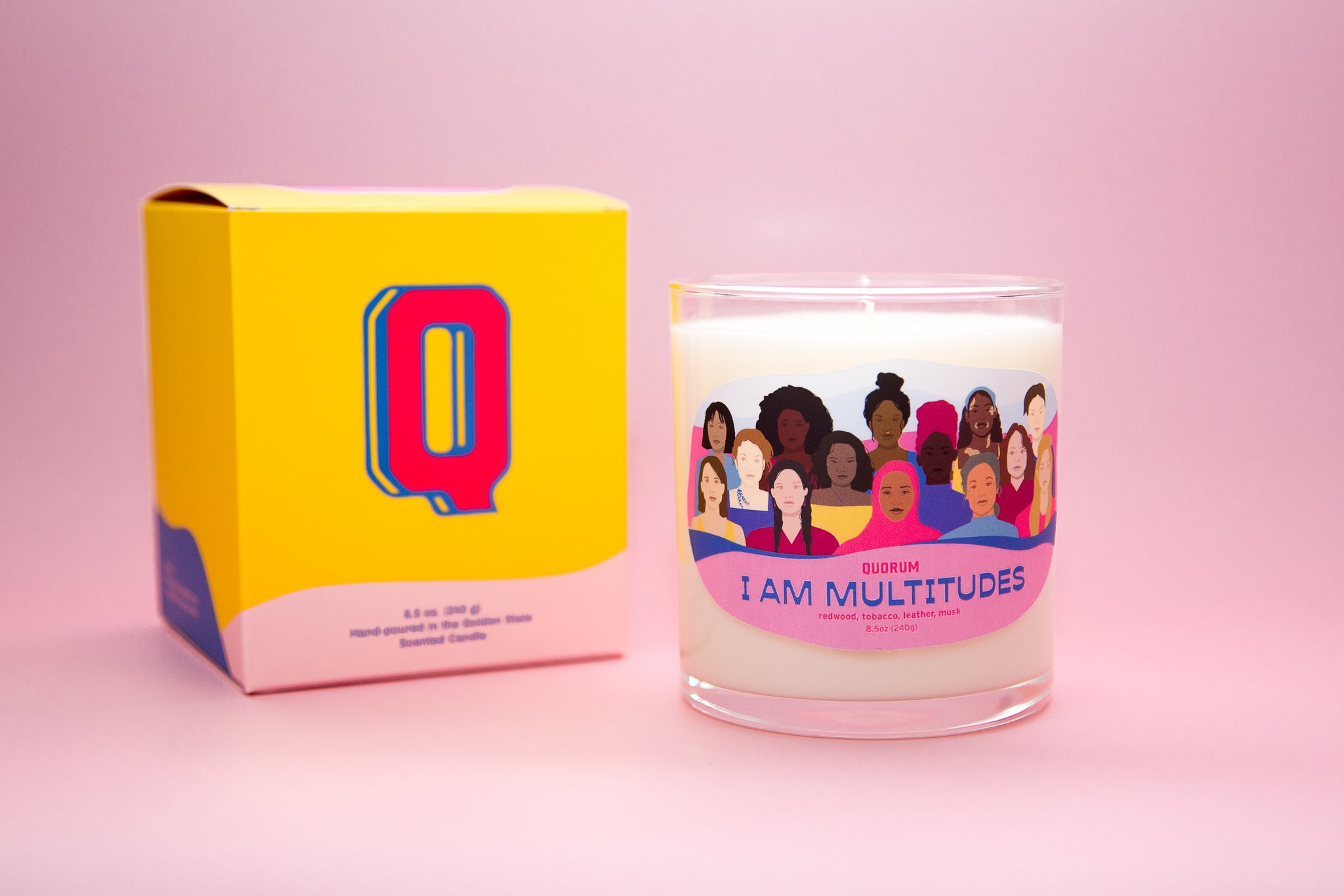 photograph of the I am multitudes affirmation candle. Photograph is on a pink background, with yellow product box next to the candle.